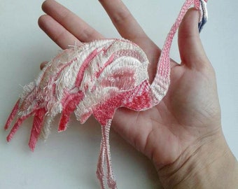 Könnte beinhalten: Ein rosa und weiß gestickter Flamingo mit langen Beinen. Der Flamingo ist aus Stoff gefertigt und hat eine flauschige Textur.