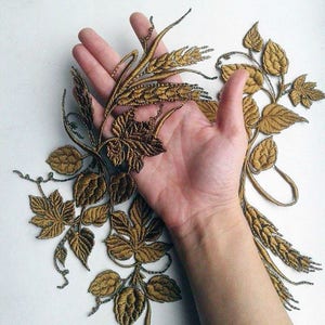 Könnte beinhalten: Gold gestickter Stoff mit einem Design aus Weizenähren und Blättern. Der Stoff ist zart und filigran, mit einem detaillierten Design.