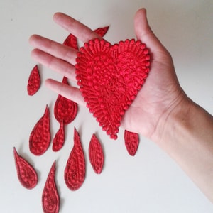 May include: Red felt heart-shaped patch with a textured surface, surrounded by smaller red felt teardrop-shaped patches.