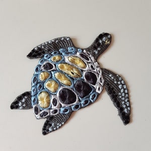 May include: An embroidered sea turtle patch in blue, black and yellow. The turtle's shell is detailed with a pattern of circles and swirls.