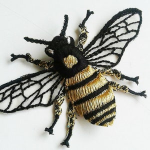 May include: A black and gold embroidered bee applique with a mesh wing design. The bee has a black body with gold stripes and a black head with white eyes.
