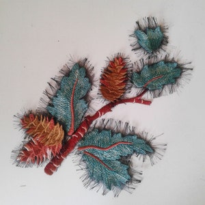 Può includere: Applique ricamato con un ramo con foglie e pigne. Le foglie sono verde acqua e verdi con cuciture rosse. Le pigne sono arancioni e marroni con cuciture bianche. Il ramo è rosso con cuciture nere.