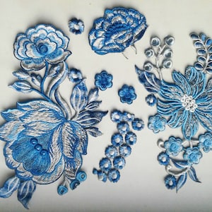 Pode incluir: Um conjunto de apliques florais bordados em azul e prata. Os apliques apresentam vários desenhos de flores, incluindo rosas, margaridas e folhas. Os apliques são perfeitos para adicionar um toque de elegância a roupas, bolsas ou decoração de casa.