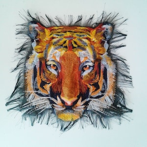 May include: Embroidered tiger face patch with a black frayed border. The tiger has orange and black stripes, white whiskers, and a black nose.