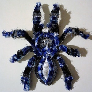 May include: A blue and black spider made of fabric with a white center. The spider is a decorative item and is made of different shades of blue and black fabric.