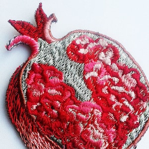 Puede incluir: Un parche bordado de granada roja con un diseño detallado. La granada está abierta, revelando las semillas en su interior. El parche es perfecto para agregar un toque de color y detalle a la ropa, las bolsas u otras manualidades.