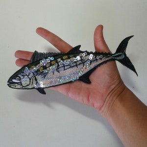 May include: A black and green embroidered fish patch with iridescent sequins. The fish has a detailed design and is perfect for adding a unique touch to clothing or accessories.