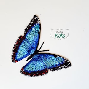 May include: Blue and green embroidered butterfly applique patch with black and red accents. The patch is perfect for adding a touch of whimsy to clothing, bags, or other crafts.