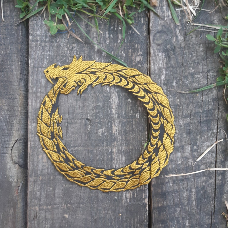 May include: A gold embroidered patch of a dragon curled into a circle. The dragon is detailed with scales and has a fierce expression.