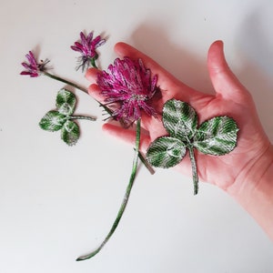 Può includere: Fiori di trifoglio fatti a mano con perline, con fiori rosa e foglie verdi e bianche. I fiori hanno lunghi steli verdi. Il trifoglio è un simbolo di fortuna ed è spesso utilizzato nell'artigianato e nelle decorazioni.