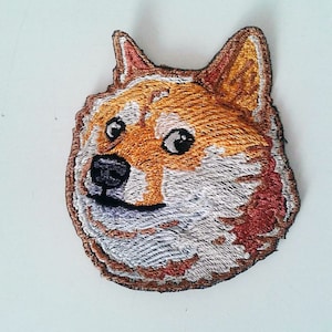 Peut inclure: Patch brodé représentant un chien Shiba Inu avec une expression surprise. Le chien a une fourrure brune, une fourrure blanche sur la poitrine et le museau, et des yeux et un nez noirs.