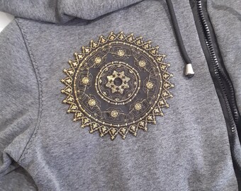 May include: A gray hooded sweatshirt with a black zipper and a gold embroidered mandala design on the front.