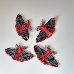May include: Four black and red embroidered moth appliques. The moths have a sheer black fabric with red embroidered details.