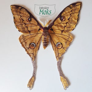 May include: Embroidered golden moth with brown accents and long tails. The moth is a decorative applique with the text "Embroidery Moks" in a green rectangle.