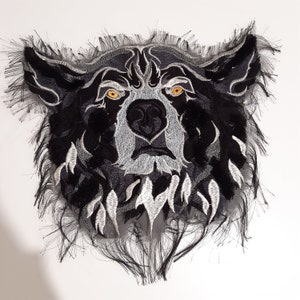 Peut inclure: Patch brodé en noir et blanc représentant une tête de loup avec un bord effiloché. Le loup a une expression féroce avec des dents acérées et des yeux jaunes brillants.