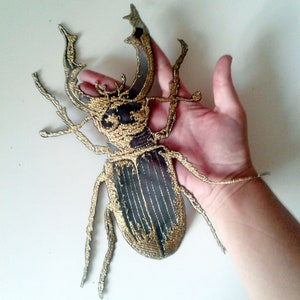 Op de afbeelding: Goud geborduurde keverpatch met zwarte details. De patch is ongeveer zo groot als een hand.