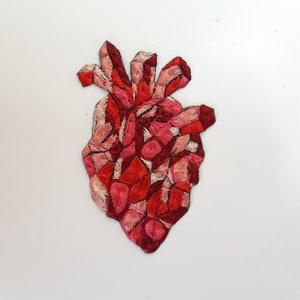 May include: A red and pink embroidered heart shaped patch. The heart is made up of many small, overlapping stitches.