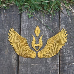 May include: Gold embroidered wings with a heart-shaped design in the center. The wings are symmetrical and have a detailed, intricate design.