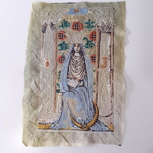 Può includere: Un'opera d'arte ricamata vintage che raffigura una donna in una veste blu seduta su un trono con una corona e una croce. L'opera è incorniciata da un bordo dorato e presenta un motivo floreale.