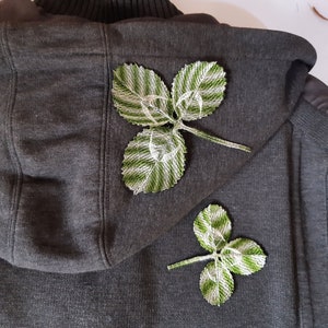 May include: Two green and white embroidered leaf patches sewn onto a dark gray hooded sweatshirt.