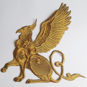 Puede incluir: Parche de hierro bordado en oro de un grifo mítico con alas detalladas y cola rizada.
