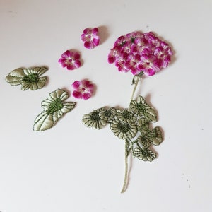 May include: Pink and white embroidered flower with green leaves. The flower is made of multiple small flowers clustered together. The leaves are delicate and have a light green color.