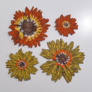 May include: Four embroidered sunflower appliques in various sizes. The appliques are in shades of orange, yellow, and brown.