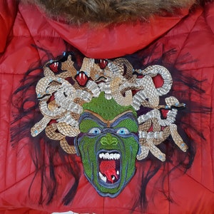 May include: Red puffer jacket with a large embroidered patch of Medusa on the back. The patch features a green face with snakes for hair and a red tongue.