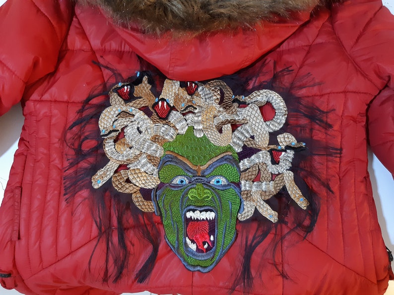 May include: Red puffer jacket with a large embroidered patch of Medusa on the back. The patch features a green face with snakes for hair and a red tongue.