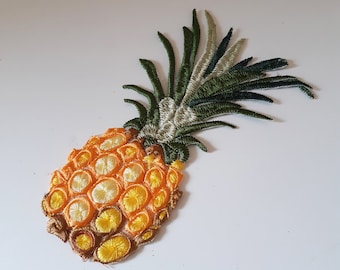 May include: A yellow and orange embroidered pineapple with green leaves. The pineapple is a decorative patch.