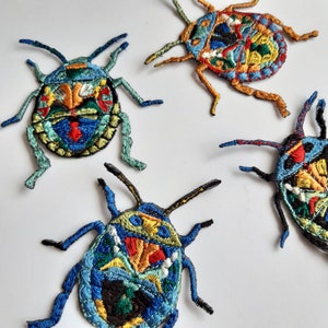 Op de afbeelding: Vier kleurrijke geborduurde strijk-op patches van insecten met ingewikkelde details. De insecten zijn blauw, groen, geel, rood en zwart.