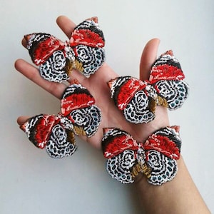 May include: Four embroidered butterfly patches in red, black, white, and gold. The butterflies are arranged in a row on a hand.