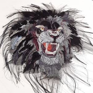 May include: A black and gray embroidered lion's head with a red open mouth and a black mane. The lion's head is on a white background.