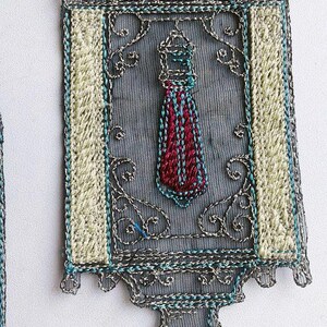 K&ouml;nnte beinhalten: Verziertes, besticktes Textil in rechteckiger Form mit dekorativer Ober- und Unterseite. Das Design zeigt ein zentrales Motiv, das einer Krawatte in Rot und Blau &auml;hnelt, umrahmt von aufwendigen silbernen und t&uuml;rkisfarbenen Stickereien.