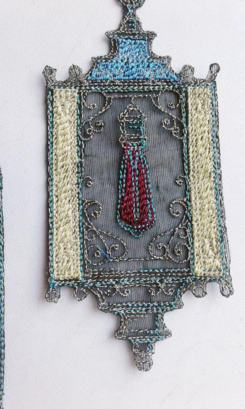 K&ouml;nnte beinhalten: Verziertes, besticktes Textil in rechteckiger Form mit dekorativer Ober- und Unterseite. Das Design zeigt ein zentrales Motiv, das einer Krawatte in Rot und Blau &auml;hnelt, umrahmt von aufwendigen silbernen und t&uuml;rkisfarbenen Stickereien.