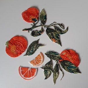 Puede incluir: Parches bordados para planchar con forma de rodajas de naranja y hojas. Los parches son en tonos verdes, naranjas y blancos.
