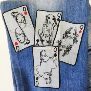 Puede incluir: Cuatro parches bordados de reinas de cartas de juego sobre un fondo de mezclilla azul. Cada parche presenta un dibujo en blanco y negro de un rostro de mujer con un símbolo de reina y un símbolo de palo en la esquina.