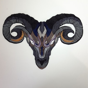 May include: Embroidered patch of a ram's head with intricate details in shades of gray, blue, and gold. The ram's eyes are white with purple accents.