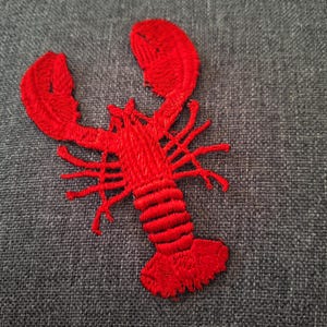 Puede incluir: Un parche bordado de langosta roja brillante. El parche presenta un diseño detallado de una langosta con sus pinzas extendidas y múltiples patas. El parche está hecho de hilo rojo, para ropa o accesorios.