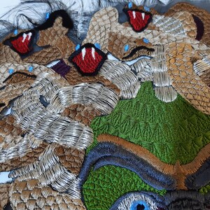 May include: Close-up of a colorful embroidered textile featuring a green, brown, and silver design with multiple red mouths and blue eyes.