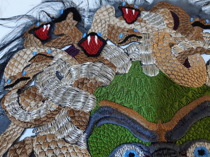 May include: Close-up of a colorful embroidered textile featuring a green, brown, and silver design with multiple red mouths and blue eyes.