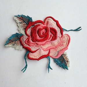 May include: A pink and red embroidered rose with green leaves. The rose is a floral design with a three-dimensional effect.