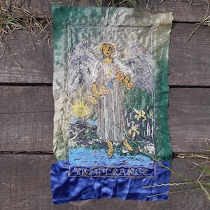 Może przedstawiać: Naszywkę z haftowanej karty tarota przedstawiającej kartę Umiarkowania. Karta przedstawia anioła wlewającego wodę z dwóch kielichów, z tekstem "TEMPERANCE" na dole.