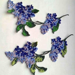 Könnte beinhalten: Drei gestickte Aufnäher mit lila und blauen Fliederblüten und grünen Blättern. Die Aufnäher sind perfekt, um Kleidung, Taschen oder anderen Bastelarbeiten einen Hauch von floralem Charme zu verleihen.