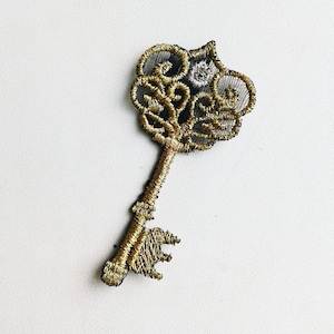May include: A gold key with a decorative, intricate design. The key is made of metal and has a black outline.