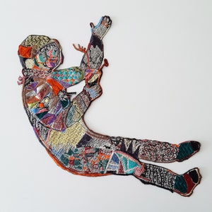 Könnte beinhalten: Eine bunte gestickte Figur einer Person mit ausgestreckten Armen und Beinen, hergestellt aus verschiedenen Stoffresten und Texturen.