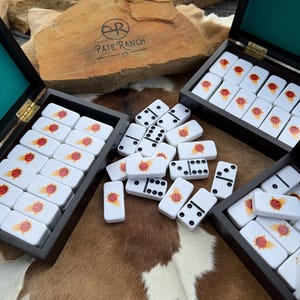 May include: Three dark wooden boxes with teal velvet interiors, each containing white dominoes featuring a basketball graphic. Scattered between the boxes are additional dominoes, some showing black pips and others displaying the basketball design.