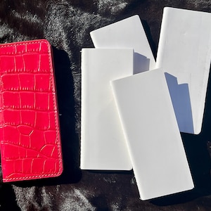 May include: A bright pink leather wallet with a crocodile pattern and five white blank notebooks.