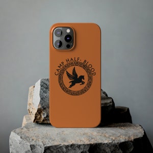 Puede incluir: Una funda de iPhone marrón con un logotipo negro de Camp Half-Blood que presenta un caballo alado y un diseño de llave griega.