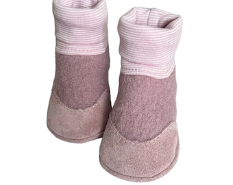 Puede incluir: Un par de botines rosas para bebé con suela de ante y un puño a rayas rosa y blanco.